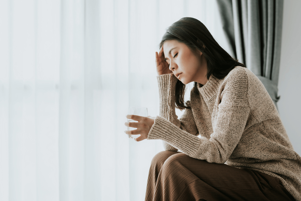 a woman sitting down and holding a hand to her head in discomfort