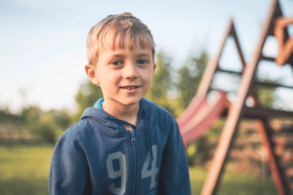 a young boy standing outside in front of a playground