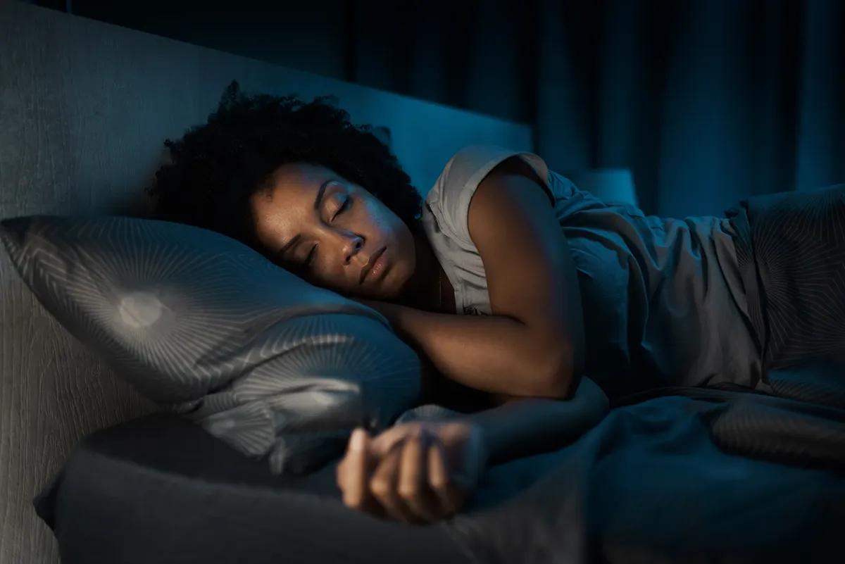 A young woman asleep in bed in a dim room.