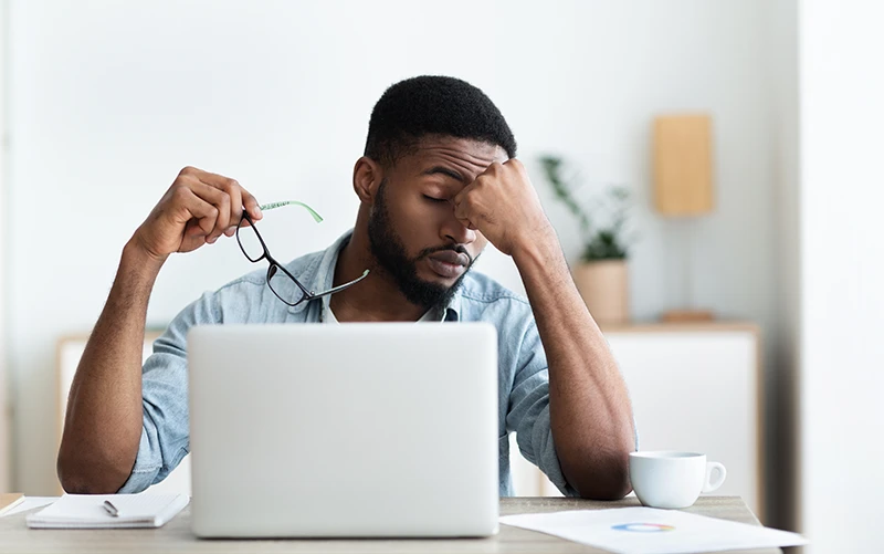 a man resting his head on his hand and looking uncomfortable while working on a laptop